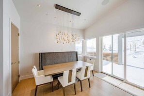 Ein moderner Essbereich mit einem Holztisch, weißen Stühlen, einer grauen gepolsterten Bank und einer außergewöhnlichen Leuchte.