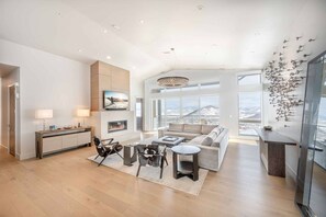 A spacious living room with a fireplace, a large window with a city view, and a modern chandelier.