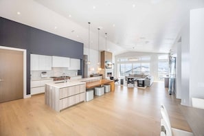A spacious kitchen with a central island, modern pendant lighting, and a view to the living area.