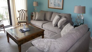 Ein Wohnzimmer mit einer Couch, Sesseln, einem Couchtisch und einem gerahmten Bild an der Wand.