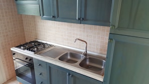 A kitchen with a gas stove, double sink, and cabinets.