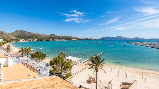 Ein Küstenblick mit Strand, klarem blauen Wasser, Booten und Bergen im Hintergrund.