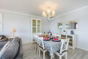 A dining area with a table set for four, white chairs, a chandelier, a cabinet with glass doors, and a mirror on the wall.