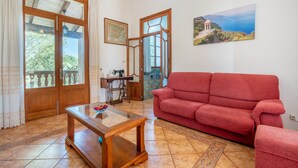 Ein Wohnzimmer mit rotem Sofa, einem Holztisch, einer Nähmaschine und einem großen Fenster mit Meerblick.