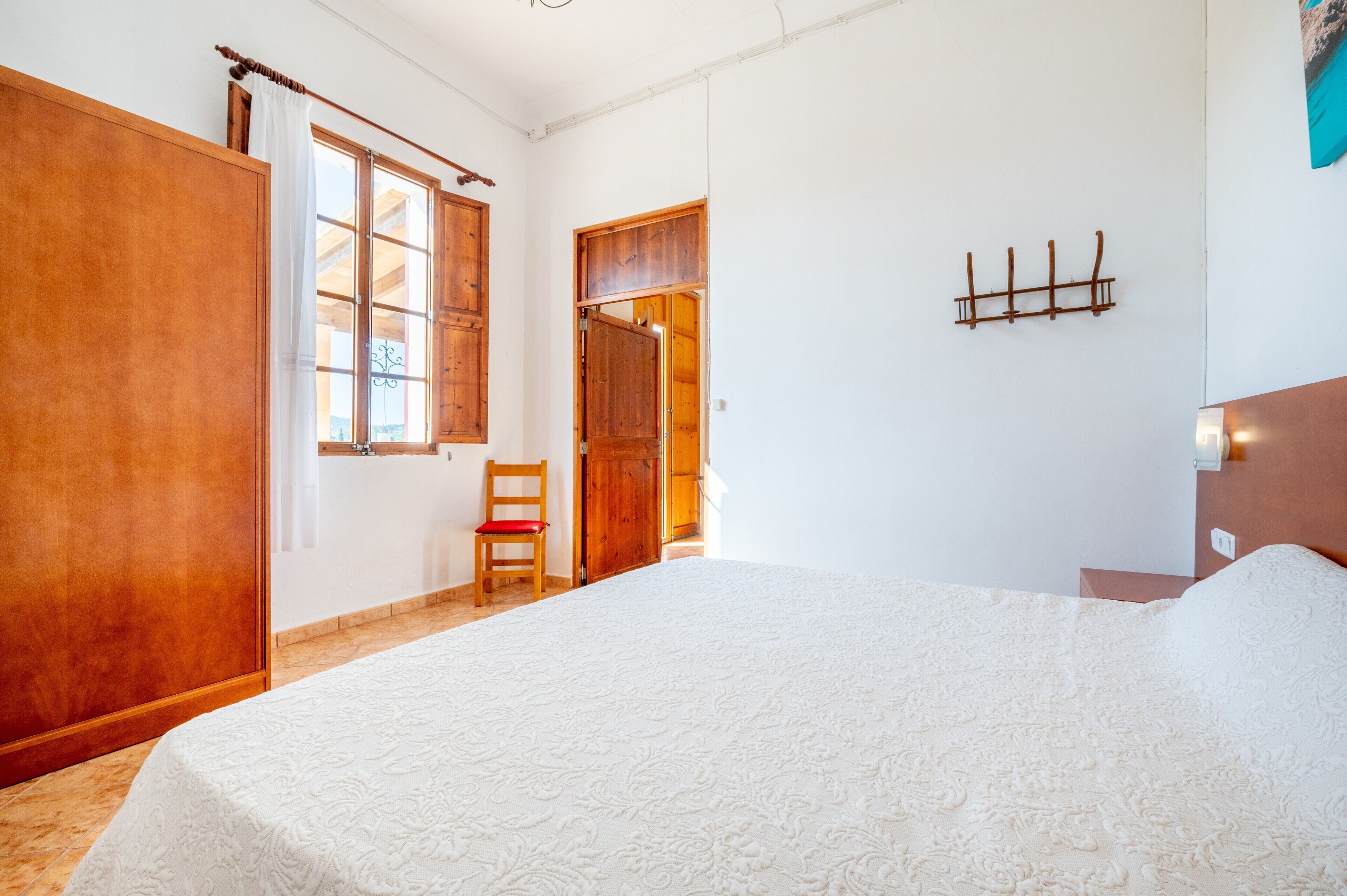 A bedroom with a large bed, a wooden wardrobe, a chair, and a wooden door.