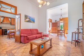 A spacious living area with a red sofa, a glass coffee table, and a dining area with wooden furniture.