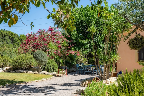 A garden with a gravel path, a small table, chairs, and a building with a window.