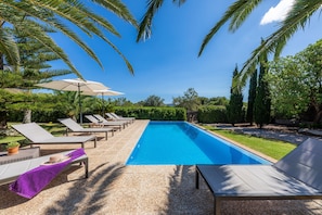 A swimming pool with lounge chairs and umbrellas, surrounded by greenery.