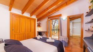 Een slaapkamer met een grote houten garderobe, een bed met donkere beddengoed, een klein tafeltje met een lamp, en uitzicht op het buitengebeuren door een deur.