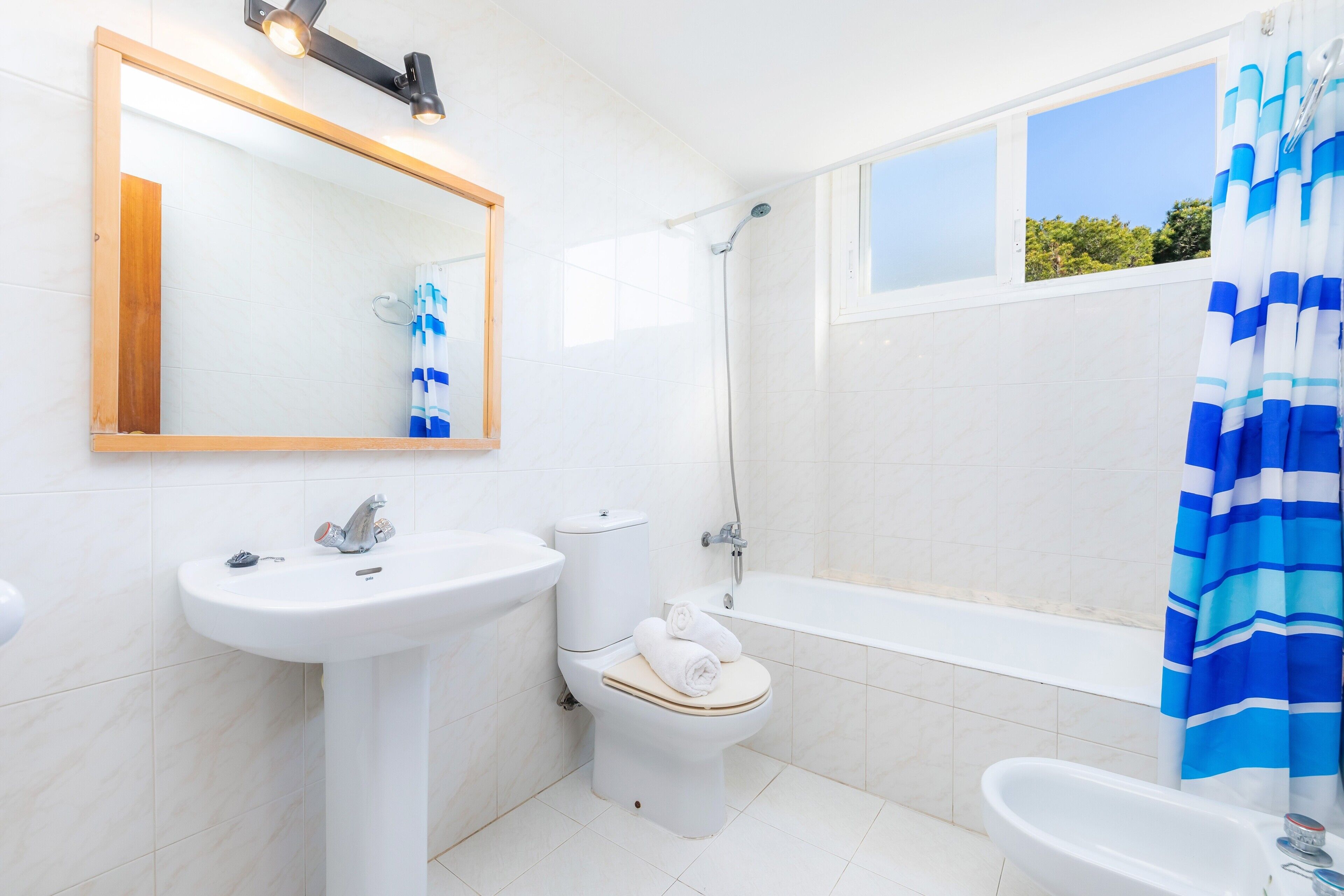 Un baño con inodoro, lavamanos, bañera y ventana con vistas a árboles.