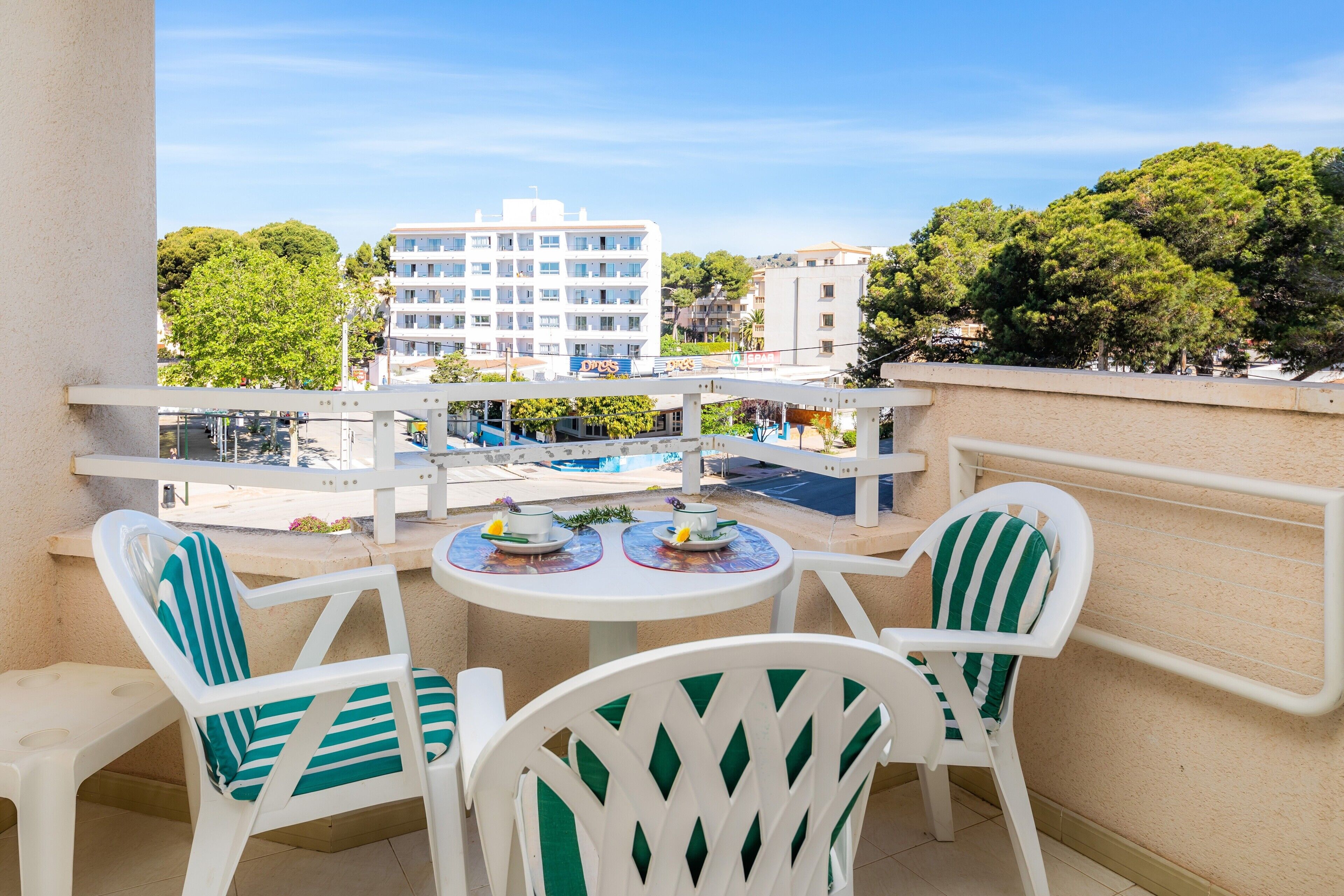 Ein Balkon mit weißen Stühlen und einem Tisch, mit Blick auf einen Pool und Gebäude.