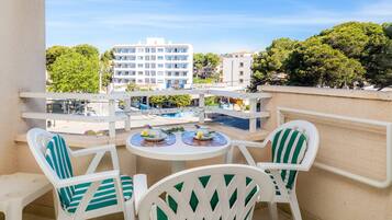Ein Balkon mit weißen Stühlen und einem Tisch, mit Blick auf einen Pool und Gebäude.