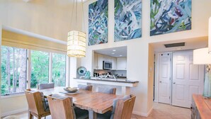 A spacious dining area with a wooden table and chairs, a kitchen with white cabinets, and abstract paintings on the wall. - Updated & Gorgeous End Unit with Spectacular Views of Pool & Sound.  South Beach Oasis Awaits you! (Hilton Head Island)