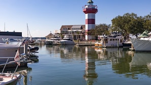 A marina with boats docked, a prominent red and white lighthouse, and a building with outdoor seating. - Updated & Gorgeous End Unit with Spectacular Views of Pool & Sound.  South Beach Oasis Awaits you! (Hilton Head Island)