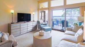 A spacious living room with a flat-screen TV, a large window, and a balcony with outdoor furniture. - Updated & Gorgeous End Unit with Spectacular Views of Pool & Sound.  South Beach Oasis Awaits you! (Hilton Head Island)
