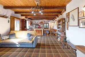 A cozy interior with a sofa, wooden ceiling, and a kitchen area. - Casa Alpinone: detached rustic house in the countryside with private garden and orchard (Crevoladossola)