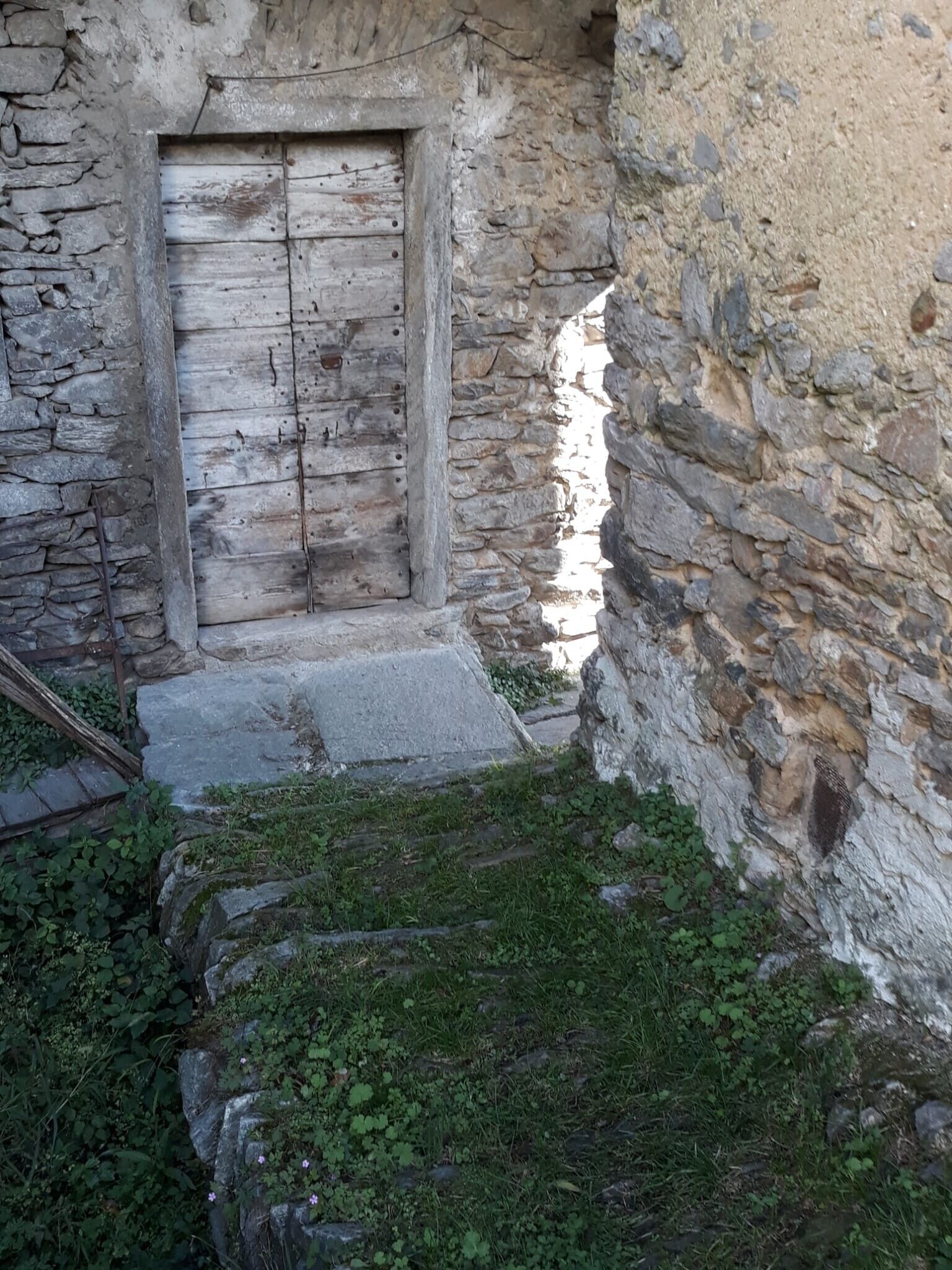 Ein Steinhaus mit einer Holztür, einer Steintreppe und einem kleinen Garten.