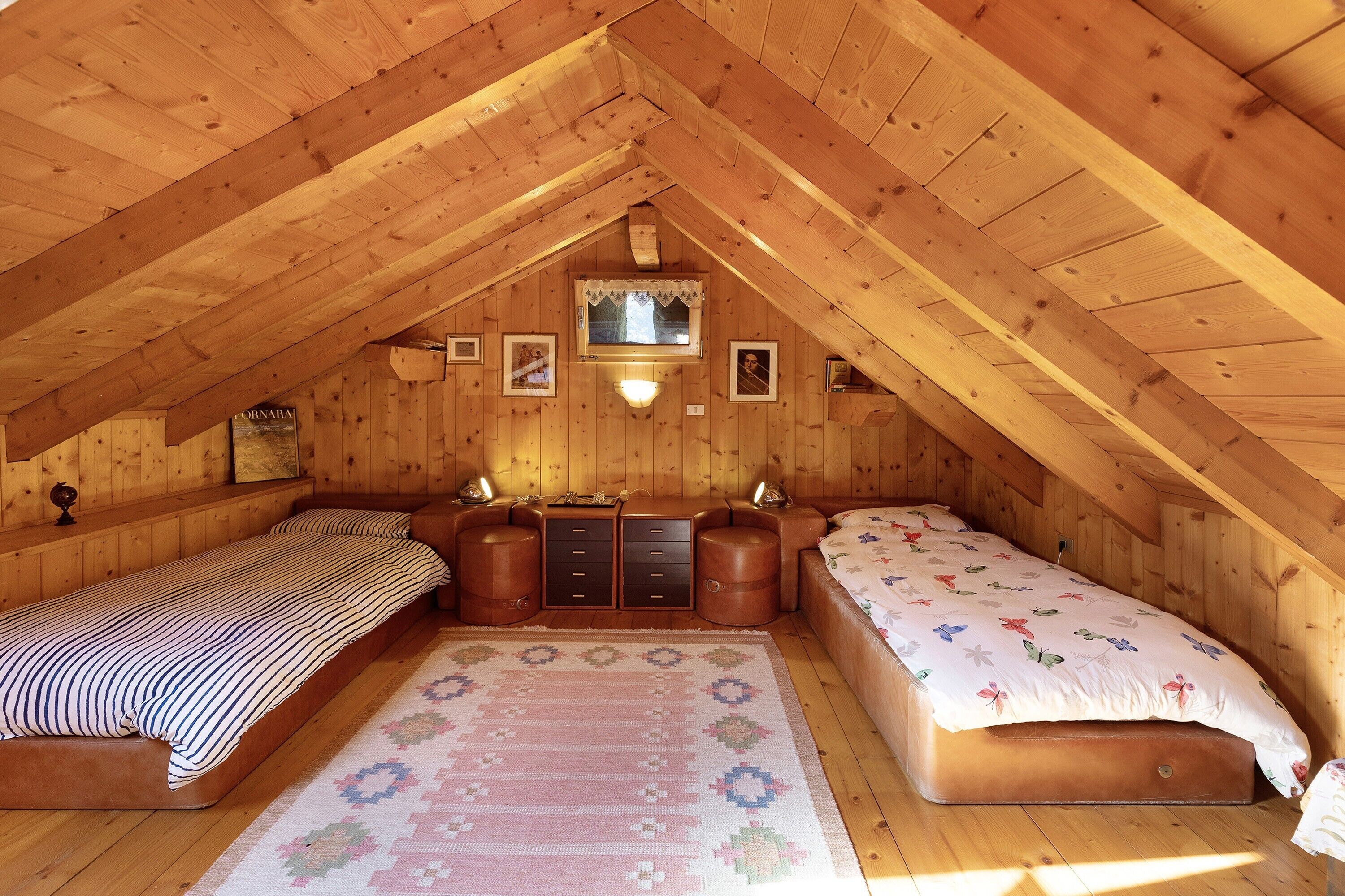 Ein gemütliches Schlafzimmer im Dachgeschoss mit zwei Betten, einem kleinen Fenster und Holzwänden.