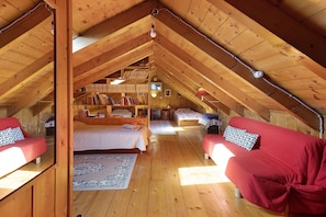 An attic room with a wooden ceiling, a bed, a sofa, a bookshelf, and a small table. - Casa Alpinone: detached rustic house in the countryside with private garden and orchard (Crevoladossola)