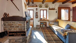 Un intérieur rustique avec une cheminée en pierre, des poutres en bois, un canapé et un tapis à carreaux.