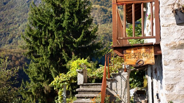 Un escalier en bois rustique mène à un bâtiment en pierre sur lequel on peut lire l’inscription « Rifugio ».