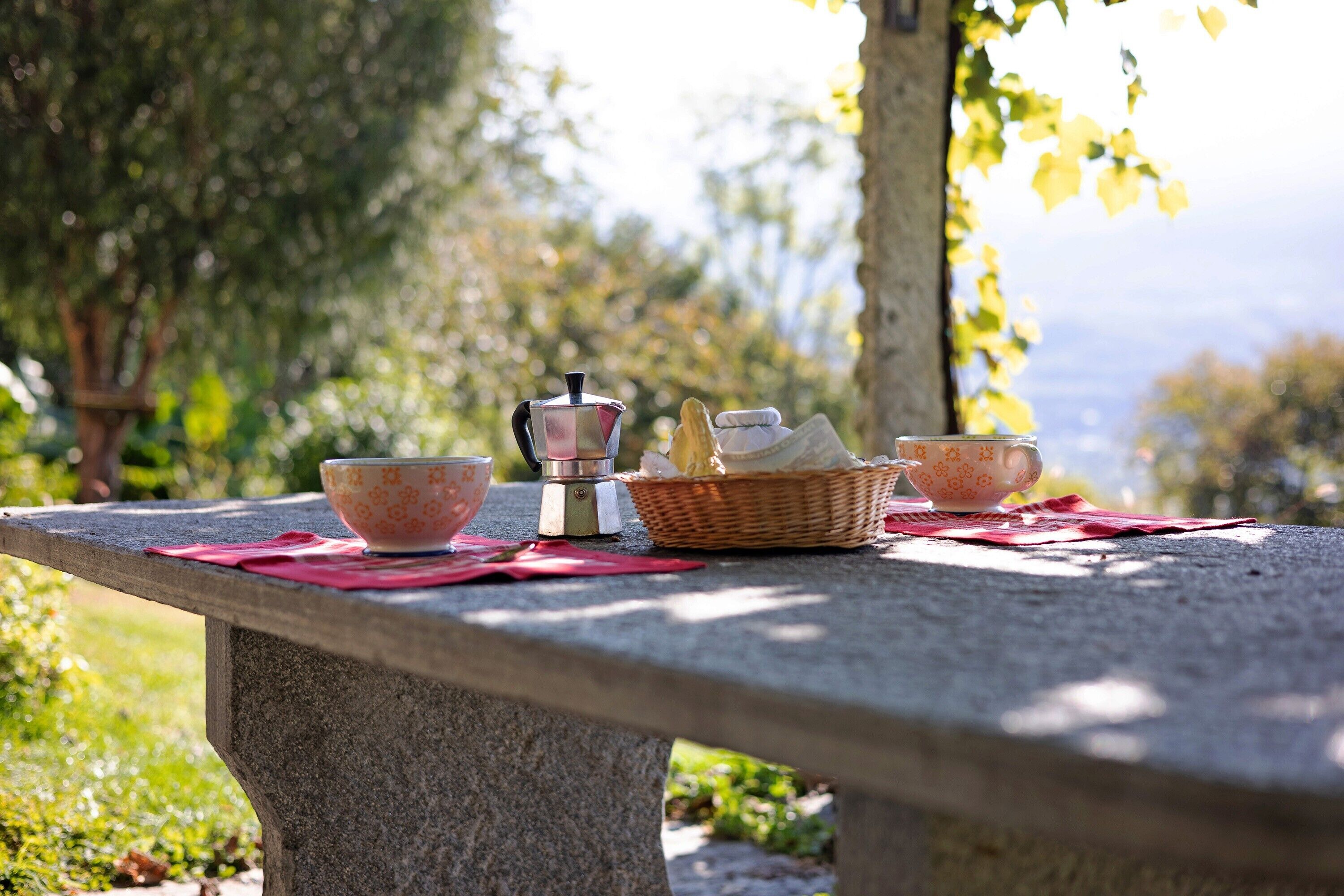 A stone bench with a basket of bread and two cups on a red cloth.