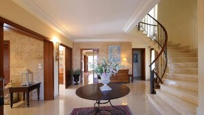 Eine geräumige Lobby mit Marmorboden, einem runden Tisch mit Blumenvasen, einer Treppe und einem großen Gemälde an der Wand.