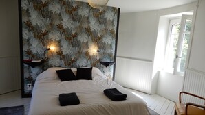 A bedroom with a large bed, two bedside tables, a wall-mounted light fixture, and a window with a view of greenery. - Castle outbuilding sleeps 6 (MORLAIX)