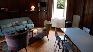 A cozy living room with a sofa, armchairs, a table, and a TV. - Castle outbuilding sleeps 6 (MORLAIX)