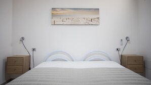 Un dormitorio con una cama, dos mesitas de noche, un cuadro colgado en la pared y dos lámparas de pared.