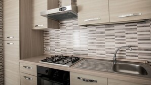 Una cocina moderna con armarios de madera, estufa a gas, horno empotrado y pileta de acero inoxidable.