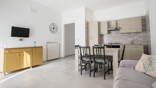 Una sala de estar moderna con comedor, televisor montado en la pared y cocina con armarios de madera y salpicadero de azulejos.