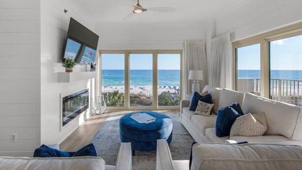 A spacious living room with a large window overlooking a beach, a ceiling fan, and a flat-screen TV mounted on the wall. - Gulf Front Condo w/Stunning Views, Private Beach Access, Gulf Front Pool! Tops'l Beach Resort (Miramar Beach)