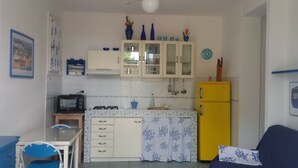 Une cuisine de taille réduite avec des meubles blancs, un réfrigérateur jaune, un four à micro-ondes et une petite table à manger avec des chaises.
