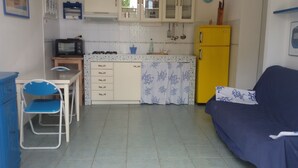 Une cuisine compacte équipée d’un four à micro-ondes, d’une cuisinière à gaz et d’un réfrigérateur jaune. On y trouve également une chaise bleue et un canapé bleu.