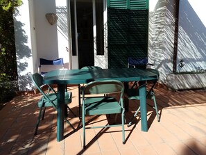 An outdoor patio with a table and chairs, a door, and a wall with a window.