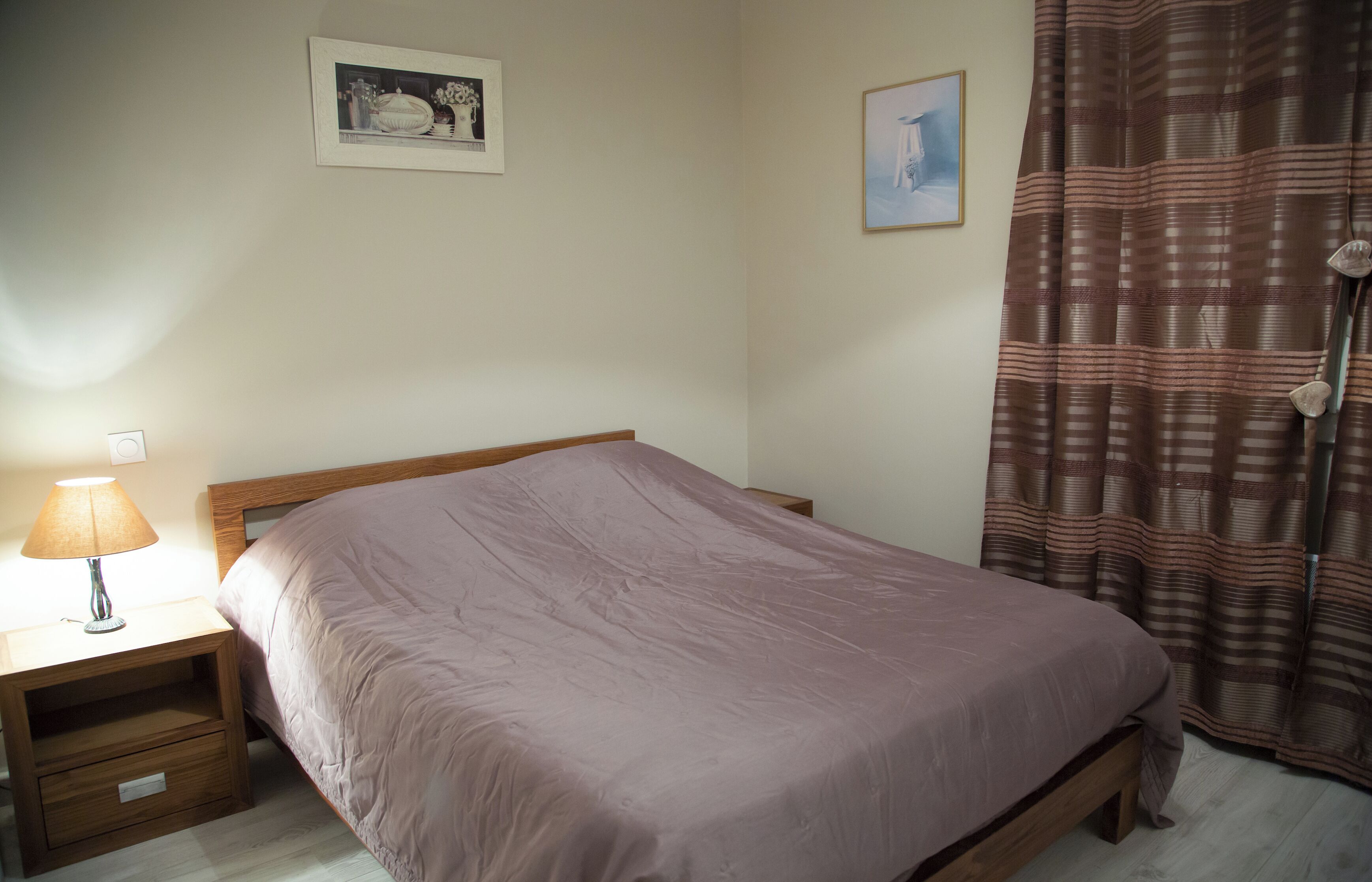 Un dormitorio con una cama, una mesita de noche, una lámpara y dos cuadros en la pared.