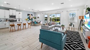 A modern kitchen with white cabinets, a central island with bar stools, and a dining area with a table and chairs. - Pool /Spa/Games Room/Movie Room/10 mins Disney/Restaurant and Bar/Modern /Chic (Kissimmee)