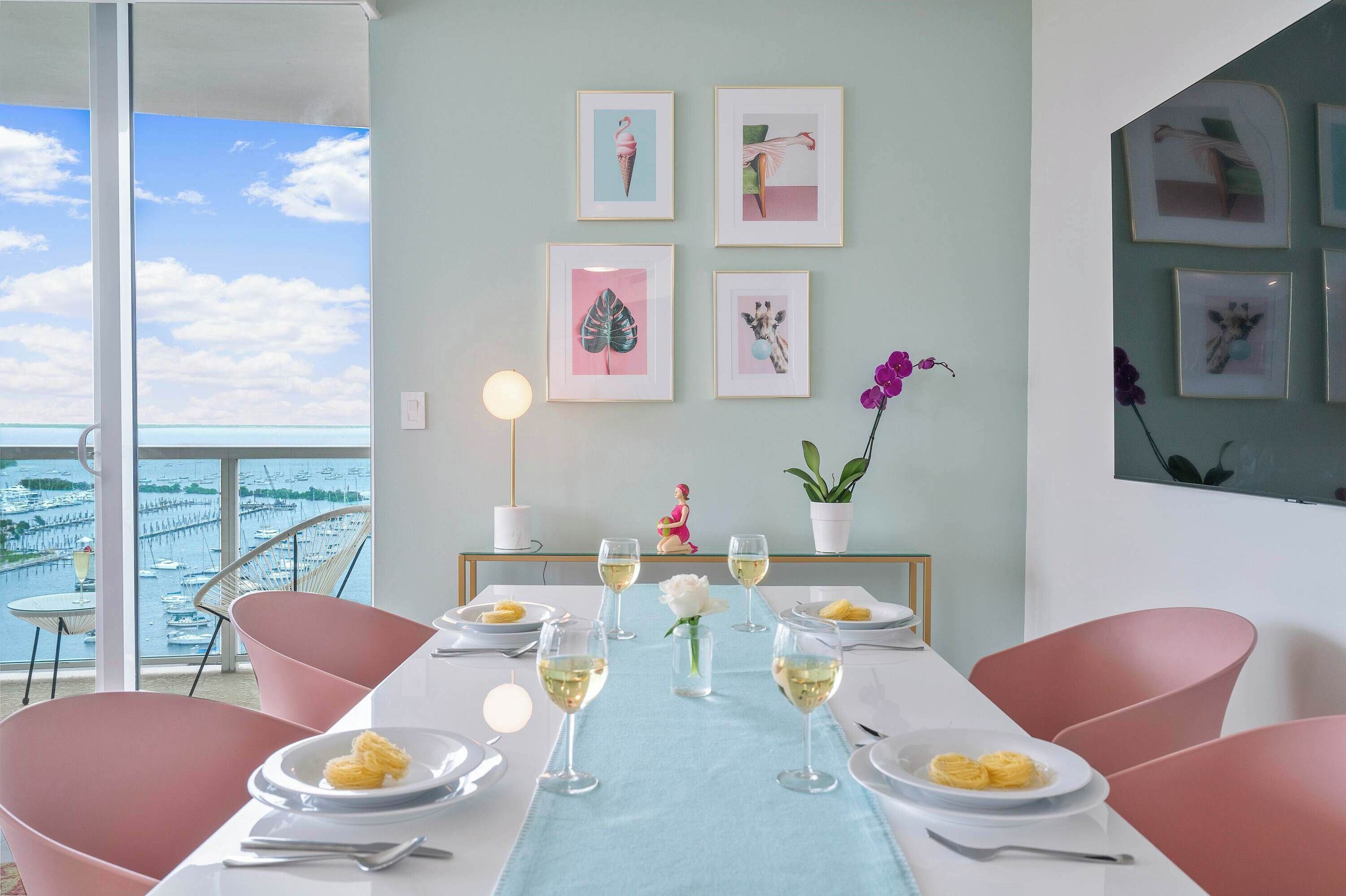 Un comedor con vistas al puerto, una mesa servida con platos y vasos, y cuadros enmarcados en la pared.
