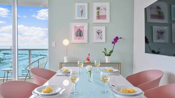 Un comedor con vistas al puerto, una mesa servida con platos y vasos, y cuadros enmarcados en la pared.