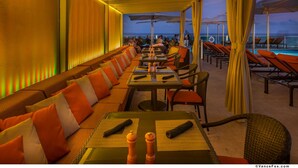 A sunlit outdoor dining area with rows of tables and chairs, overlooking a pool and a scenic view. - Panoramic Views Residence with Private Balcony (Miami)