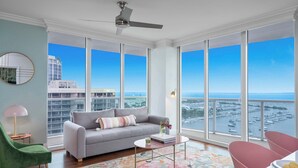 A spacious living room with a grey sofa, a green armchair, and a coffee table. Large windows offer a view of the marina and buildings. - Panoramic Views Residence with Private Balcony (Miami)