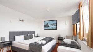 Et hotelværelse med en dobbeltseng, en enkeltseng, et maleri af et fyrtårn og et fjernsyn på væggen.