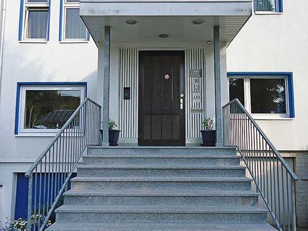 Een gebouw met een voordeur, een trap en twee potplanten aan weerszijden.
