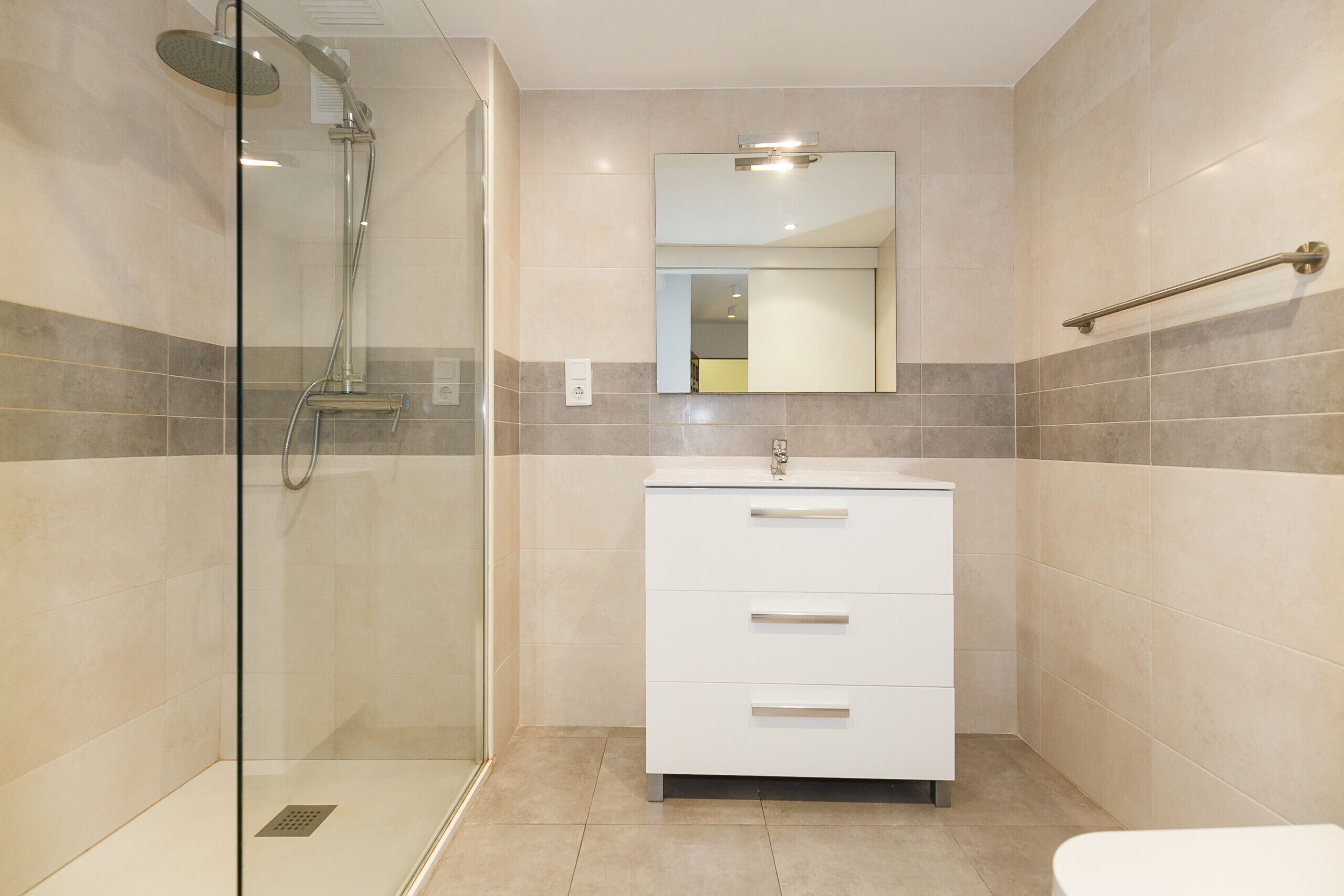 Een moderne badkamer met een douchecabine van glas, een witte wastafel met lades en een spiegel boven de wastafel.