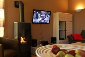 A living room with a fireplace, a television mounted on the wall, and a dining table with apples.