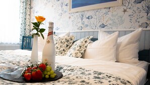 Uma cama bem arrumada com roupa de cama florida, um vaso com uma única rosa e uma garrafa de champanhe.