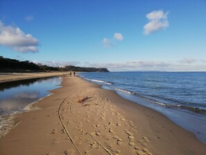En bred, sandet strand med fodspor, der fører ned mod vandet, et roligt hav og en klar himmel.