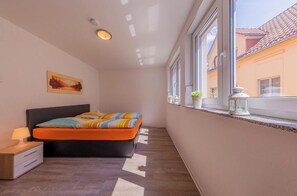 Une chambre à coucher comprenant un lit, une table de chevet, une lampe et une fenêtre donnant sur des immeubles.