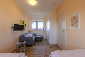 A compact hotel room with a sofa, a small table, a TV, and a window with curtains. - Hafenmeisterei 8, Deutschland (Waren (Müritz))